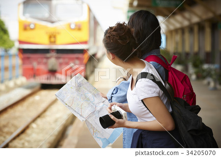 two female travelers are standing and waiting for the train near railway two female travelers are standing and waiting for the train near railway 34205070