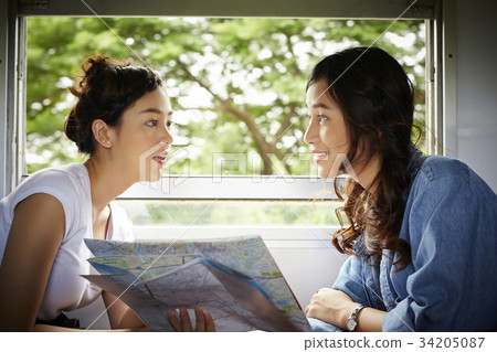 two lovely female travelers are watching map and talking together on train 34205087