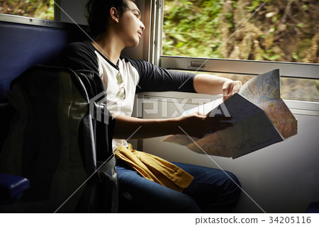 An Asian man is holding a map and looking out of the train. 34205116
