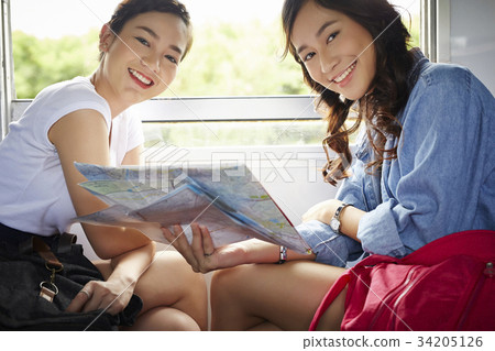 Two Asian girls are sitting on a train and smiling with the camera. Two Asian girls are sitting on a train and smiling with the camera. 34205126