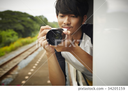 An Asian man is taking photos from the train. 34205159