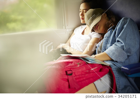 Two young girls are feeling tired when travelling by train. 34205171