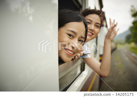 Two Asian women are looking at something from the train and waving hands. 34205175