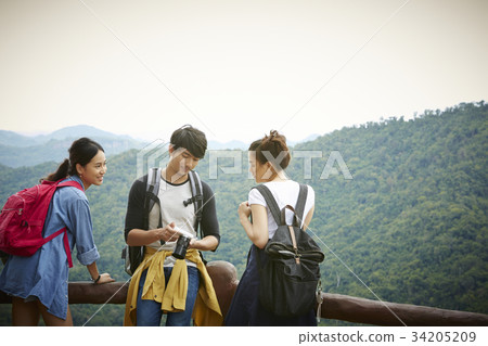 Three travellers are reviewing some photos outdoors. 34205209