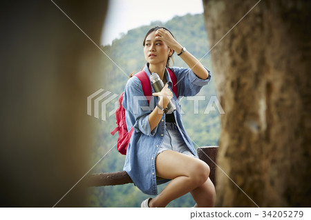 the female traveller is holding a bottle and sitting on a fence the female traveller is holding a bottle and sitting on a fence 34205279