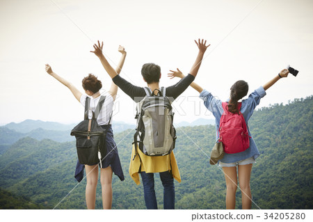 Three people are standing on the top of the mountain and raising hands 34205280