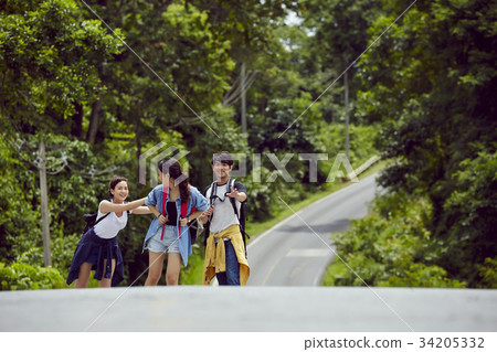 three young asian travellers are joking while walking on a road in forest 34205332