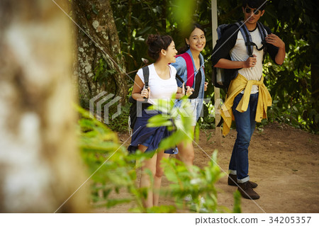 three travellers are smiling, walking and talking together in forest 34205357