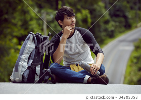 a handsome man with a bottle of water is sitting on the road 34205358