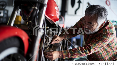 Senior man repairing a motorcycle Senior man repairing a motorcycle 34211821
