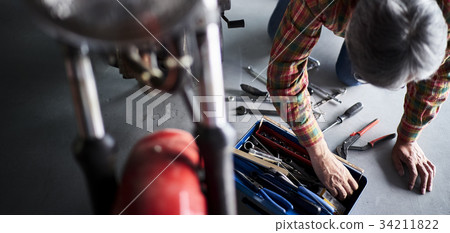 Senior man repairing a motorcycle Senior man repairing a motorcycle 34211822