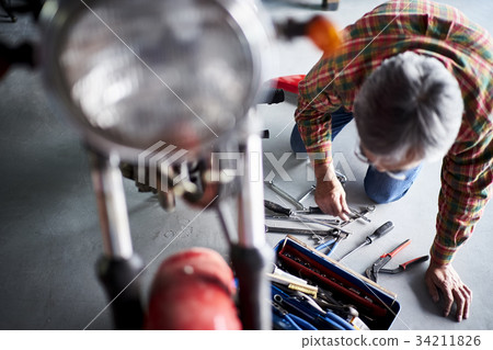 Senior man repairing a motorcycle Senior man repairing a motorcycle 34211826