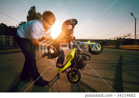 Trainer teaches small bikers to do stunts on a motorcycle 34214682
