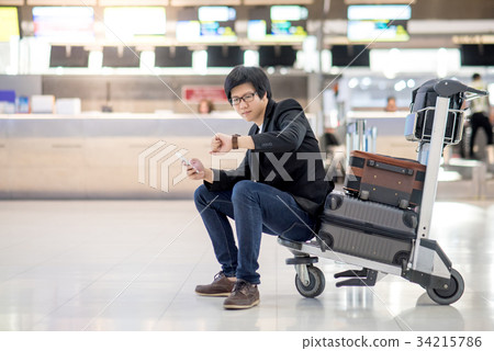 Asian man sitting on trolley in airport terminal 34215786