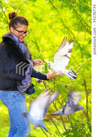 Beautiful woman feeding pigeons in the park Beautiful woman feeding pigeons in the park 34236734