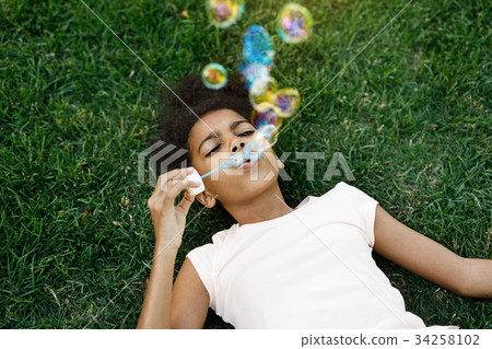 Girl lying on grass blowing bubbles in the air 34258102