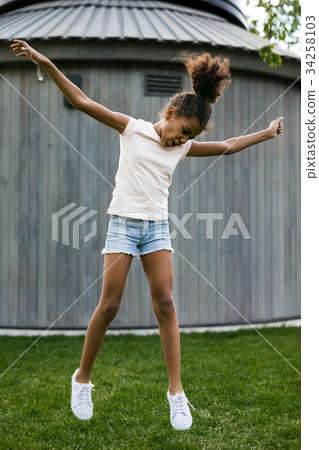 Cheerful girl jumping on grass at backyard Cheerful girl jumping on grass at backyard 34258103