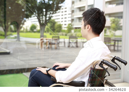 Young man sitting on a wheelchair and looking out Young man sitting on a wheelchair and looking out 34264628