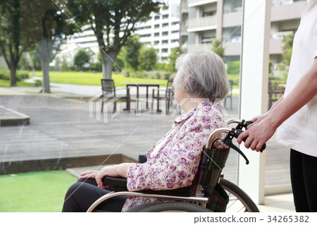 Elderly woman attending a care helper while looking at the courtyard 34265382