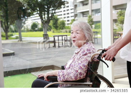 Elderly woman attending a care helper while looking at the courtyard 34265385
