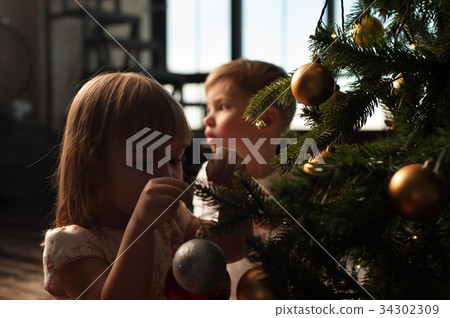 Two caucasian children sitting near Christmas tree 34302309