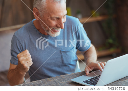 Overjoyed aged man using his laptop Overjoyed aged man using his laptop 34310728