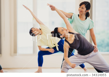 Young woman and instructor doing yoga in yoga studio Young woman and instructor doing yoga in yoga studio 34314955