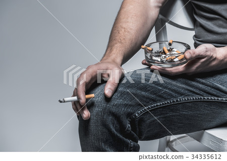 Man holding ashtray with stubs near legs 34335612