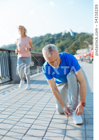 Pleasant senior man tying shoelaces while his wife Pleasant senior man tying shoelaces while his wife 34338289
