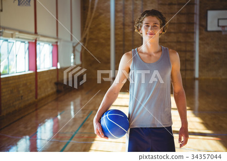 Portrait of smiling young man with basketball standing in court Portrait of smiling young man with basketball standing in court 34357044