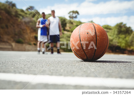 Orange basketball on ground with player standing in background 34357264