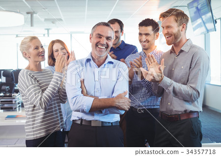 Happy businessman standing with arms crossed while colleagues clapping Happy businessman standing with arms crossed while colleagues clapping 34357718