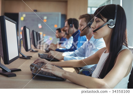 Side view of businesswoman typing on keyboard at call center Side view of businesswoman typing on keyboard at call center 34358100