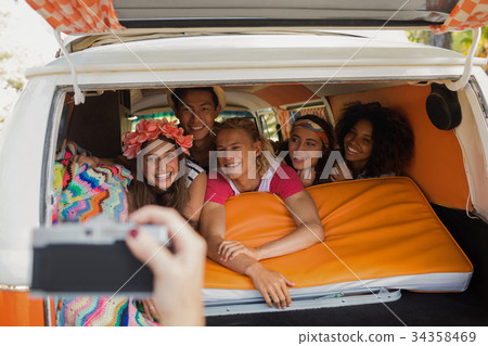 Cropped hand photographing smiling friends in camper van Cropped hand photographing smiling friends in camper van 34358469