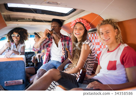 Portrait of smiling friends holding beer bottles together in camper van Portrait of smiling friends holding beer bottles together in camper van 34358586