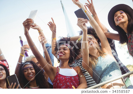 Low angle view of friends taking selfie through their mobile phones at music festival Low angle view of friends taking selfie through their mobile phones at music festival 34358587