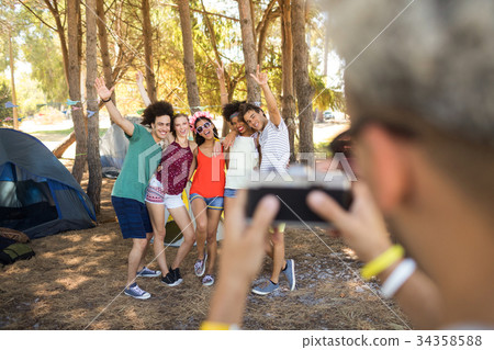 Man photographing friends at campsite Man photographing friends at campsite 34358588