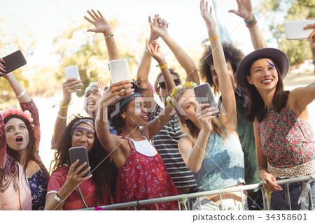 Smiling friends taking selfie through their mobile phones at music festival Smiling friends taking selfie through their mobile phones at music festival 34358601
