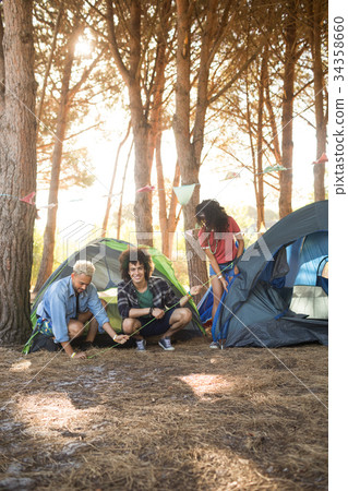 Happy man with friends setting up tent on field Happy man with friends setting up tent on field 34358660