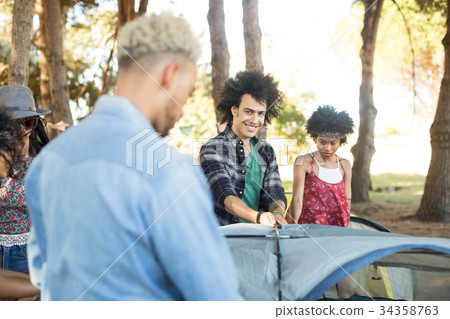 Smiling man with friends setting up tent Smiling man with friends setting up tent 34358763