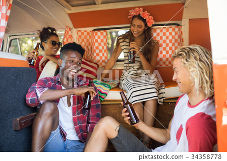 Happy friends sitting while holding beer bottles in camper van Happy friends sitting while holding beer bottles in camper van 34358778