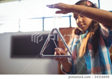 Girl playing triangle in classroom Girl playing triangle in classroom 34358899