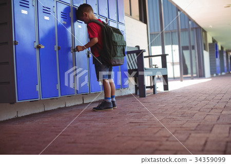 Full length of boy leaning on lockers in corridor 34359099