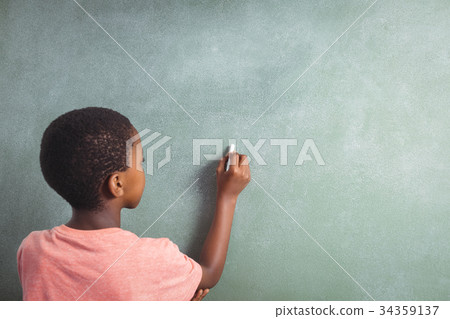 Boy writing with chalk on greenboard in school Boy writing with chalk on greenboard in school 34359137