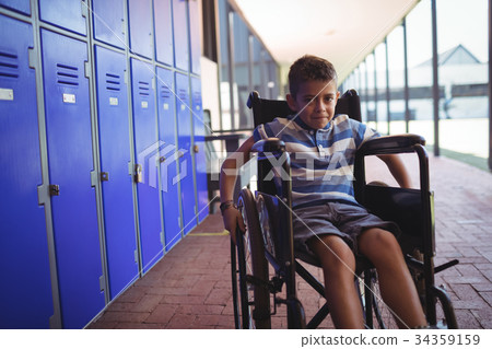 Portrait of boy sitting on wheelchair by lockers in corridor 34359159