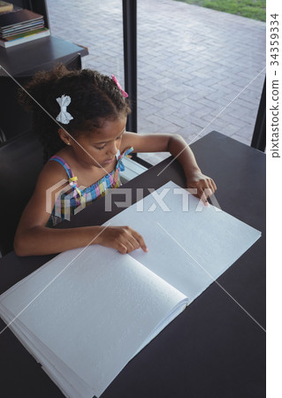 Girl reading braille at desk in library 34359334