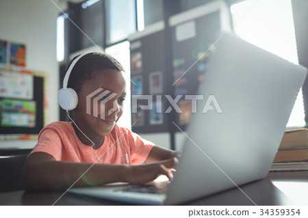 Boy listening music while using laptop Boy listening music while using laptop 34359354