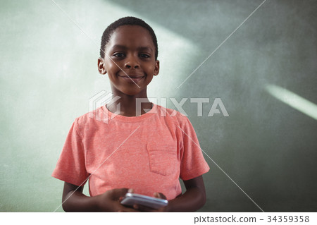 Smiling boy holding cellphone against greenboard Smiling boy holding cellphone against greenboard 34359358