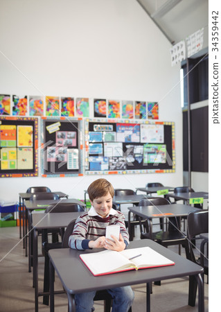 Boy using mobile phone while sitting at desk 34359442