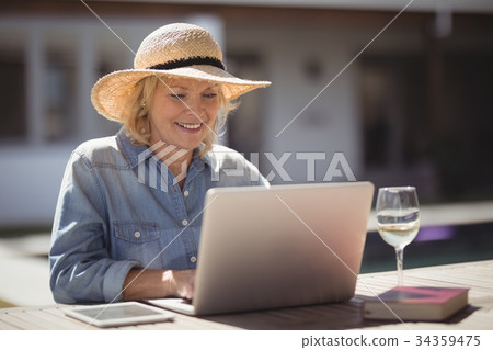Senior woman using her laptop outside house Senior woman using her laptop outside house 34359475